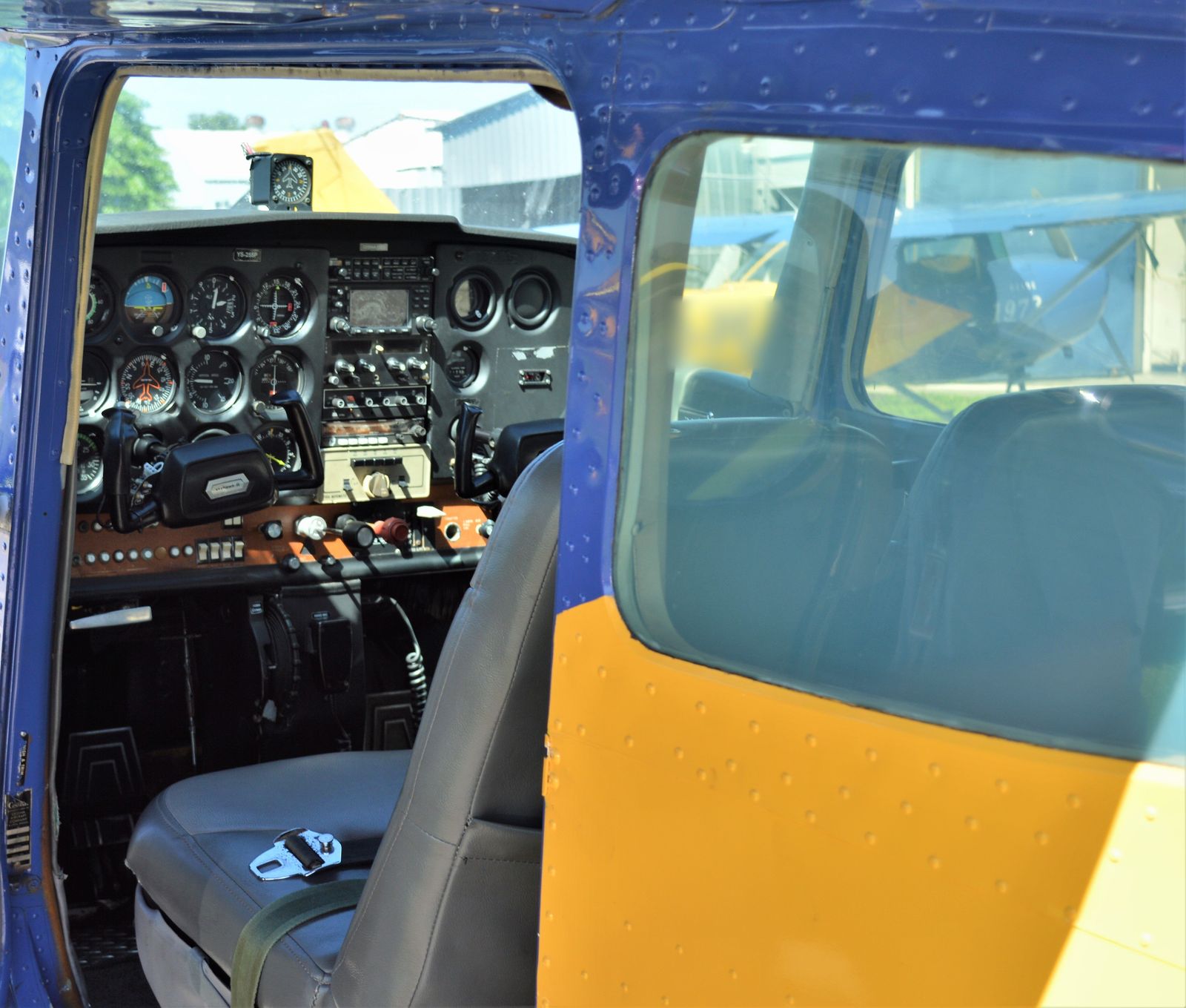 The instrument panel and grey front seats of a blue and yellow single-engine aircraft, seen through the open door.