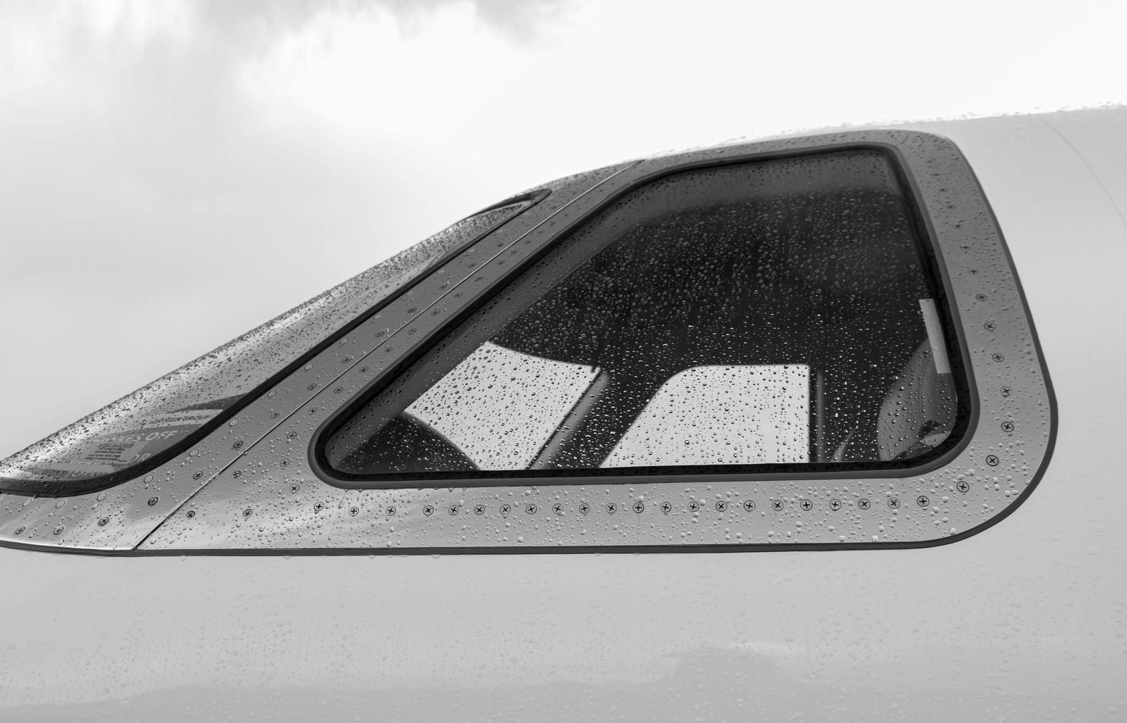 Water drops beaded on the cockpit side window of a white aircraft, in black and white.