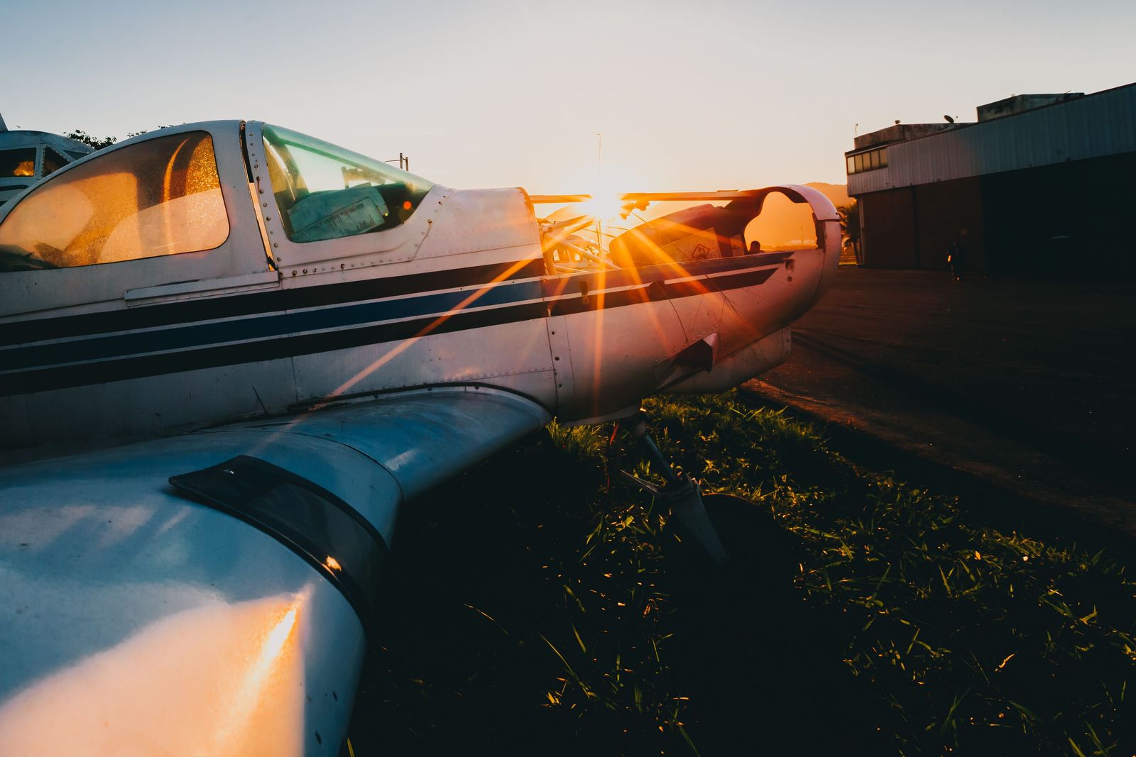 Low sun flaring across the wing and striped fuselage of a light aircraft, with light pooling on the wing surface.