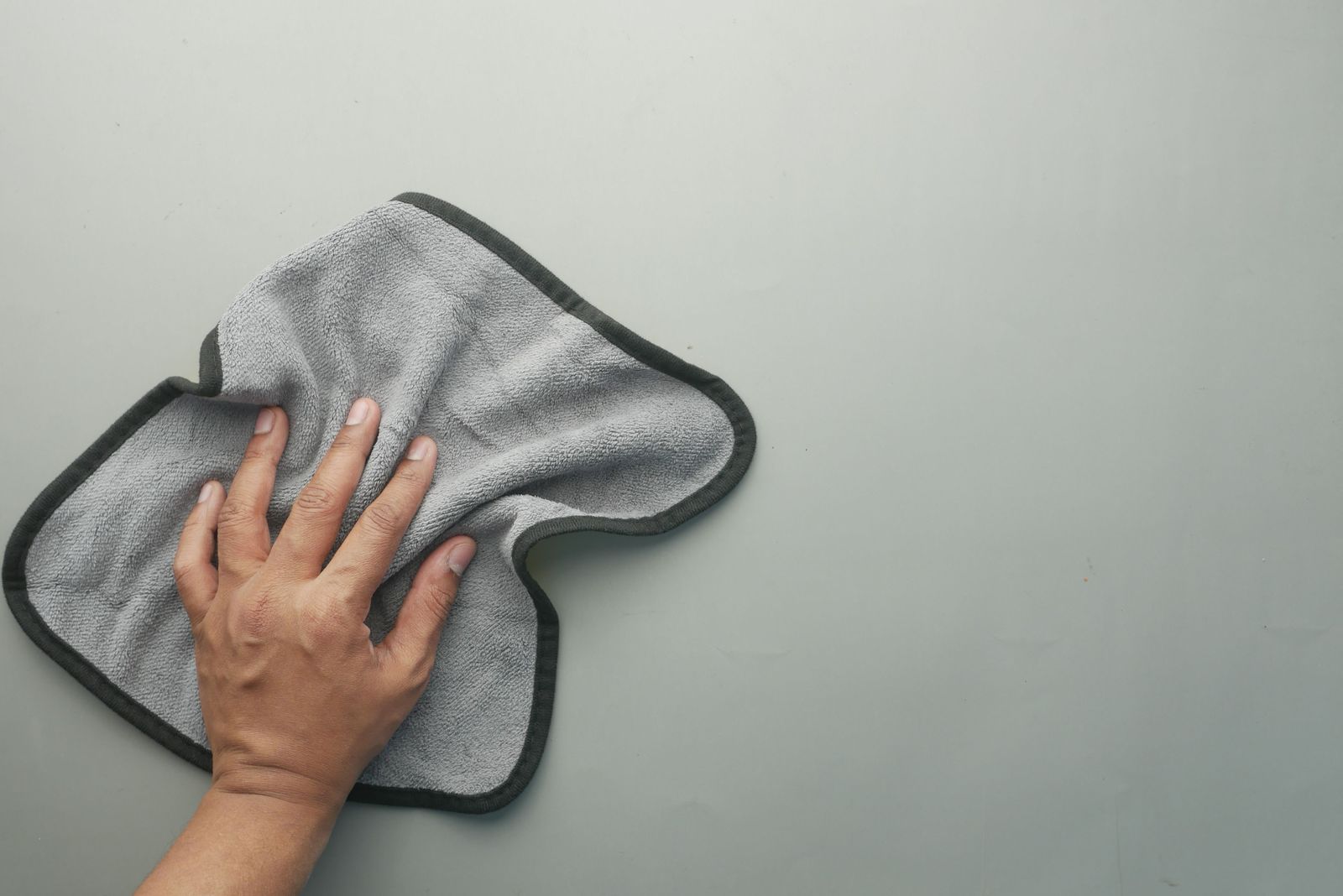 A hand wiping a smooth, pale surface with a folded grey microfiber cloth.
