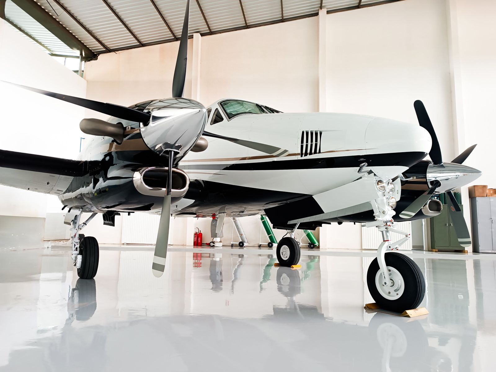 A white and black twin turboprop reflected in the glossy floor of a bright hangar.