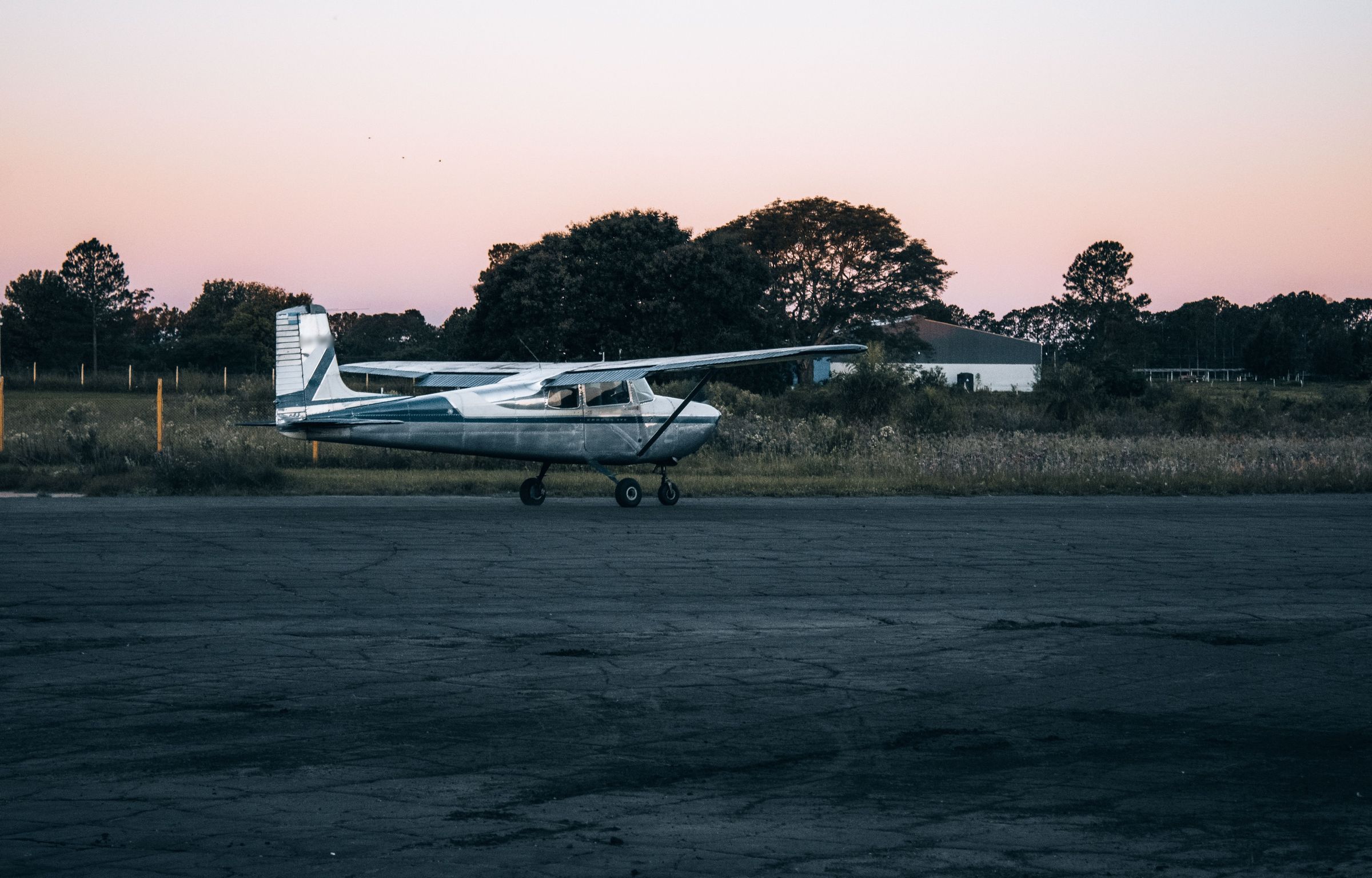 A polished aluminum high-wing single-engine aircraft parked on a quiet ramp under a pink dusk sky.
