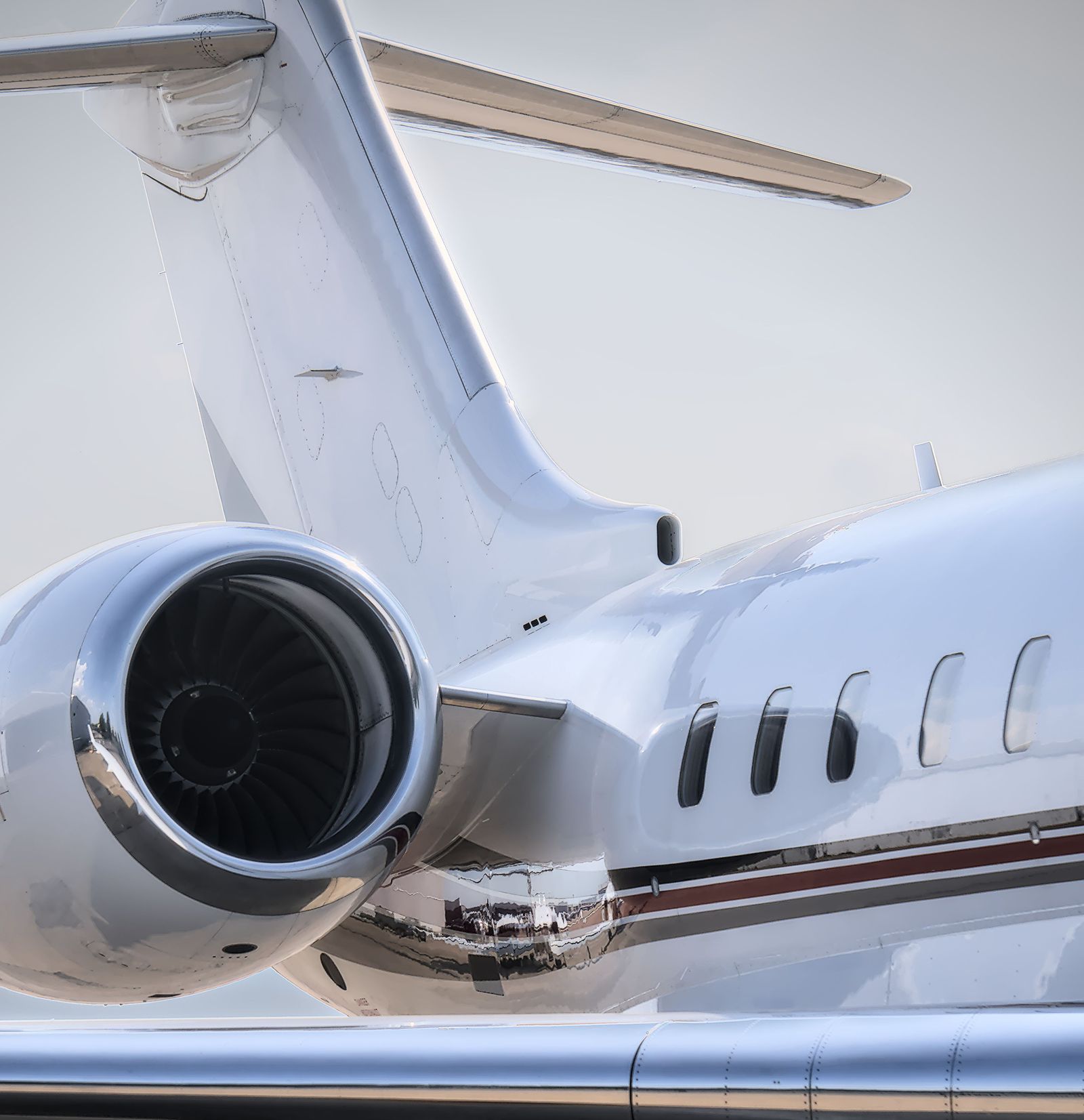 Close view of a large business jet's rear engine, tail and cabin windows, the glossy white paint reflecting the ramp.