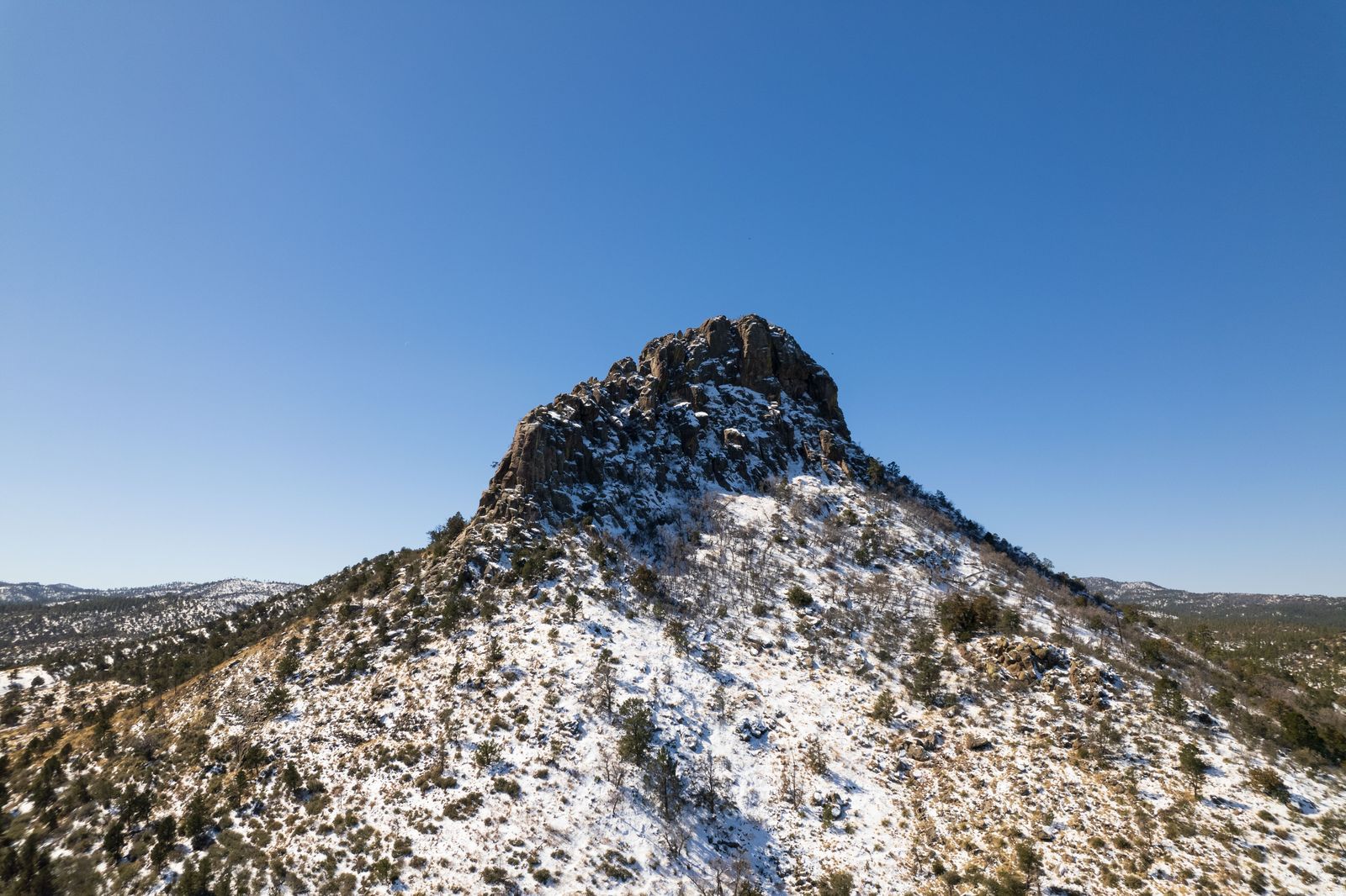 Thumb Butte near Prescott, Arizona, dusted with snow under a clear, deep blue sky.