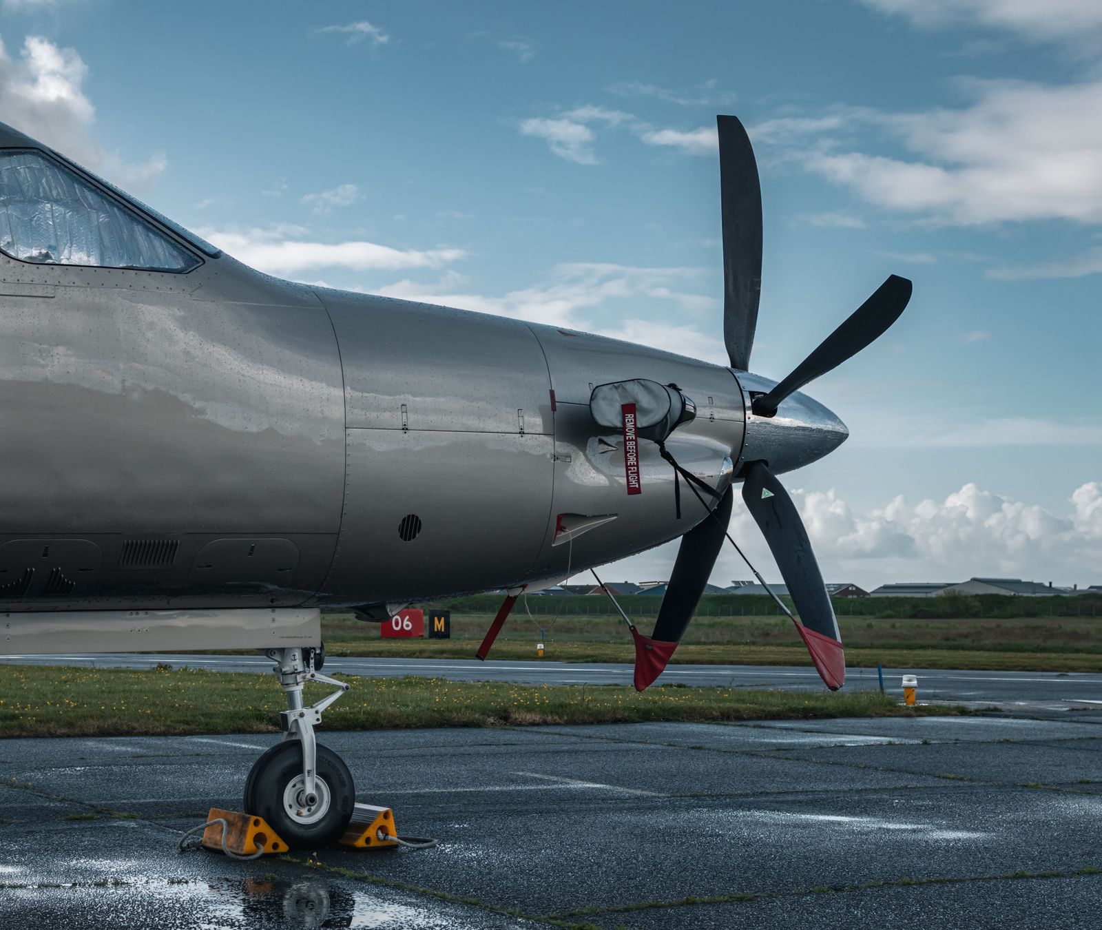 Rain beading on the polished grey nose and five-blade propeller of a turboprop parked on a wet ramp.